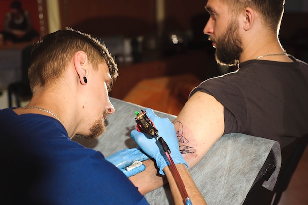 Tattooist robi tatuaż. Mężczyzna tworzy obraz pod ręką z nim w salonie.