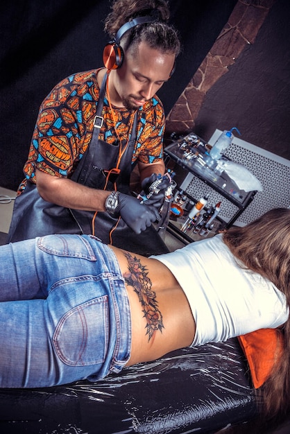 Tattooist wykonuje tatuaż na skórze swojego klienta w salonie tatuażu.