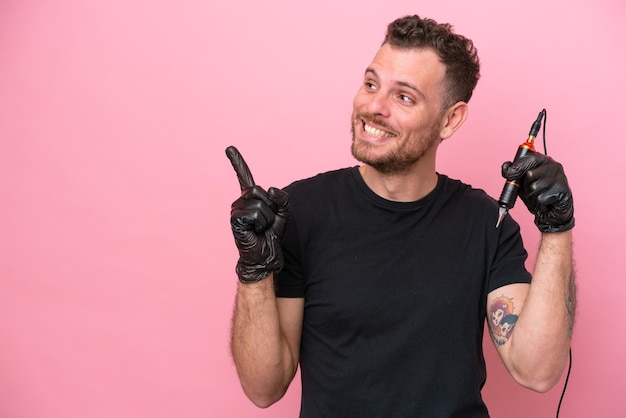 Tatuażysta brazylijski mężczyzna na białym tle na różowym tle zamierzający zrealizować rozwiązanie, podnosząc palec w górę