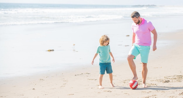 Tatuś z dzieckiem chłopiec w weekend letni dzień rodzinny tata i dziecko bawią się na świeżym powietrzu dzieciństwo i rodzicielstwo rodzinne wakacje sport aktywność kopia przestrzeń szczęśliwy ojciec i syn grają w piłkę nożną na plaży