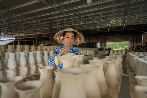 Tay Ninh WIETNAM JUL 06 2023 Kobieta pracująca w fabryce ceramicznej Stok surowych małych kubków ceramicznych na półce kształt kubka ceramicznego tradycyjny proces produkcji kubków keramicznych w fabrii