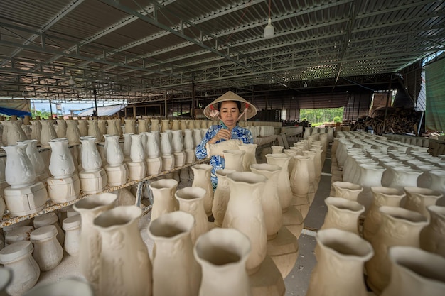 Tay Ninh WIETNAM JUL 06 2023 Kobieta pracująca w fabryce ceramicznej Stok surowych małych kubków ceramicznych na półce kształt kubka ceramicznego tradycyjny proces produkcji kubków keramicznych w fabrii