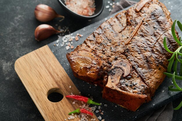 Tbone stek lub porterhouse Tbone stek lub porterhouse w sosie z przyprawami solą i rozmarynem na czarnej płycie ceramicznej na betonowym tle Widok z góry Miejsce na tekst