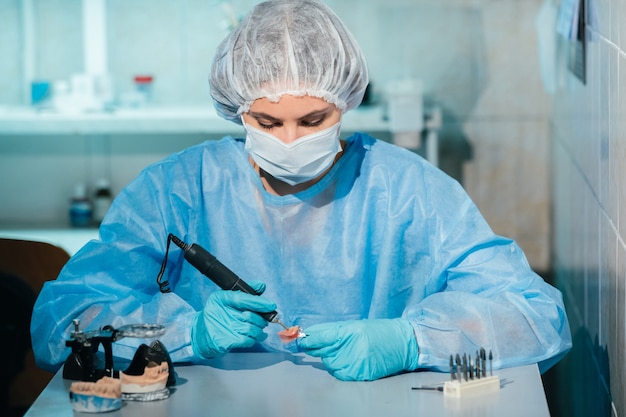 Technik dentystyczny w masce i rękawiczkach pracuje nad protezą zęba w swoim laboratorium