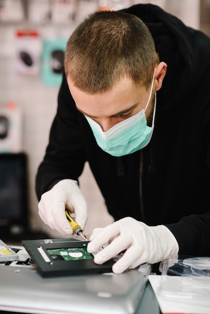 Technik naprawia laptop w laboratorium. Koncepcja naprawy komputera, elektroniki, aktualizacji, technologii. Koronawirus. Obsługuje działanie, będący ubranym maskę ochronną w warsztacie.