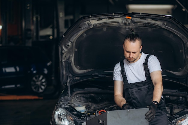 Technik sprawdza system klimatyzacji samochodu, ładuje płyn chłodniczy, naprawca trzyma narzędzie monitorujące, aby sprawdzić i naprawić system klimatyzacyjny samochodu, naprawa klimatyzacji