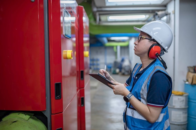 Technik utrzymania ruchu w ciepłowni Pracownicy petrochemii nadzorują pracę rurociągów gazowych i naftowych w fabryce Inżynierowie zakładają ochronniki słuchu W pomieszczeniu z wieloma rurami