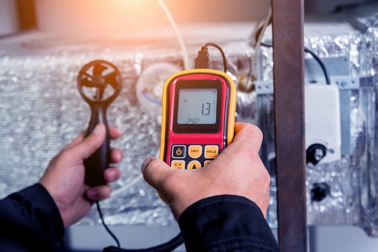 Zdjęcie technik używa ręcznego anemometru do pomiaru przepływu powietrza, prędkości i ciśnienia wiatru.