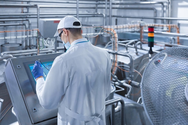 Technolog ustawia linię produkcyjną stojąc przy cyfrowym ekranie na wydziale mleczarni