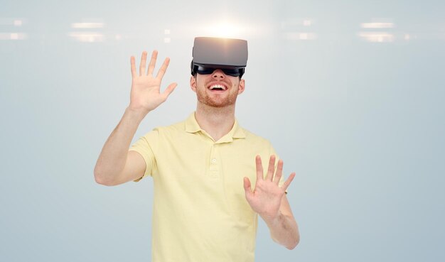Technologia 3D, wirtualna rzeczywistość, rozrywka i koncepcja ludzi - szczęśliwy młody człowiek z zestawem słuchawkowym wirtualnej rzeczywistości lub okularami 3D grający w grę na szarym tle