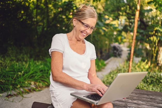 Technologia, Koncepcja Osób Starszych - Osoby Starsze Szczęśliwy Starszy Starsza Kobieta Pracuje Online Z Laptopa Na Zewnątrz W Ogrodzie. Praca Zdalna, Edukacja Na Odległość.