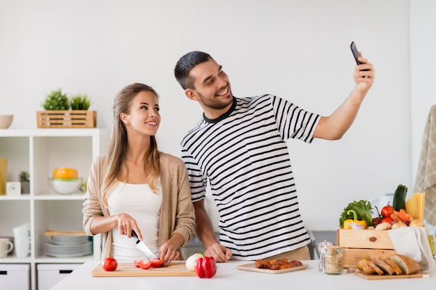Technologia ludzi i koncepcja jedzenia szczęśliwa para gotująca jedzenie i robiąca selfie w kuchni domowej
