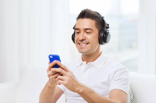 technologia, ludzie, styl życia i koncepcja uczenia się na odległość - szczęśliwy człowiek ze smartfonem i słuchawkami do słuchania muzyki w domu