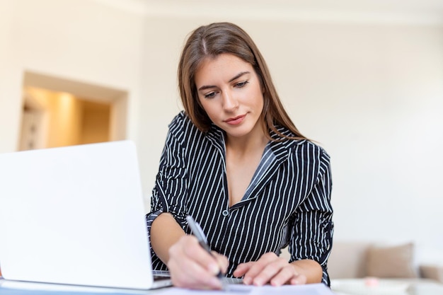 Technologia pracy zdalnej i koncepcja ludzi szczęśliwa uśmiechnięta młoda kobieta biznesu z laptopem i papierami pracującymi w domowym biurze podczas kryzysu zdrowotnego Covid19