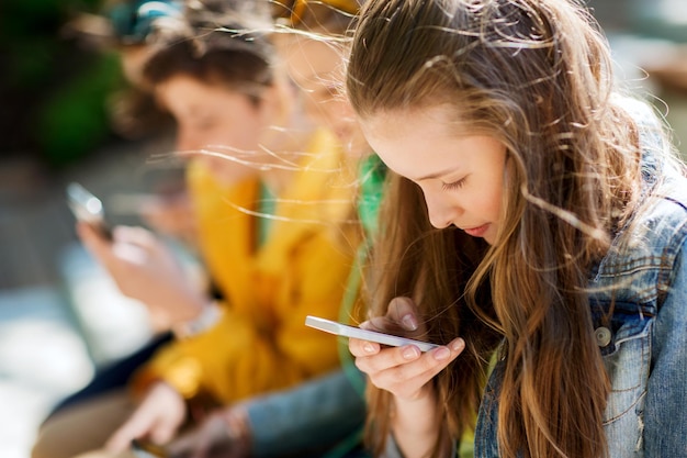 technologia, uzależnienie od internetu i koncepcja ludzi - szczęśliwi nastoletni przyjaciele ze smartfonami na zewnątrz