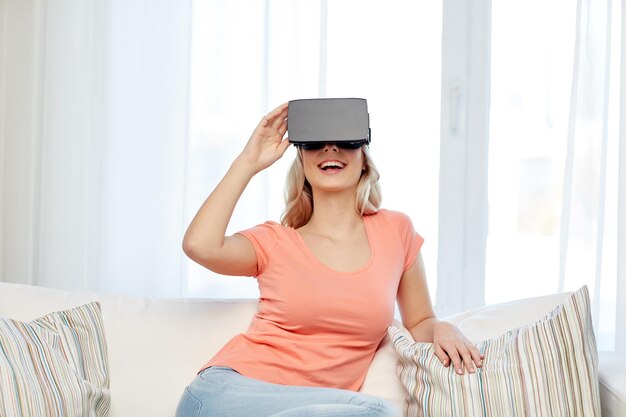 technologia, wirtualna rzeczywistość, cyberprzestrzeń, rozrywka i koncepcja ludzi - szczęśliwa młoda kobieta z zestawem słuchawkowym wirtualnej rzeczywistości lub okularami 3d siedząca na kanapie w domu