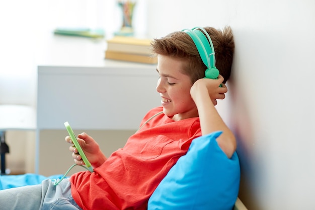 Zdjęcie technologie dzieci i ludzie koncepcja szczęśliwy uśmiechnięty chłopiec ze smartfonem i słuchawkami słuchający muzyki w domu