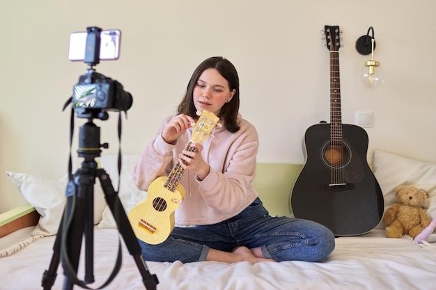 Teen dziewczyna gra na ukulele. Blog, kanał muzyczny, vlog, dziewczyna ucząca się online, rozmawiająca z obserwującymi i grająca muzykę