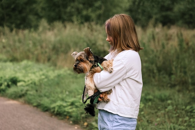 Teen dziewczyna na spacerze w letnim parku ze swoim zwierzakiem Yorkshire terrier. Dziecko wyprowadza psa