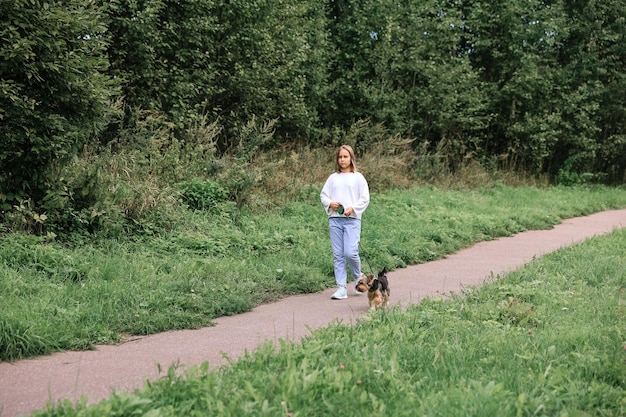 Teen dziewczyna na spacerze w letnim parku ze swoim zwierzakiem Yorkshire terrier. Dziecko wyprowadza psa