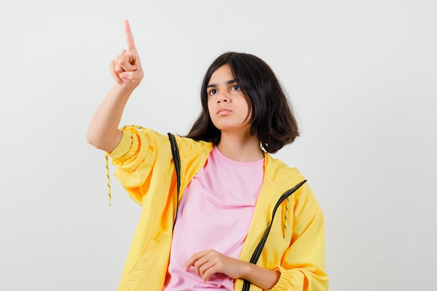 Teen dziewczyna wskazując palcem w żółty dres, t-shirt i patrząc tęsknie, widok z przodu.