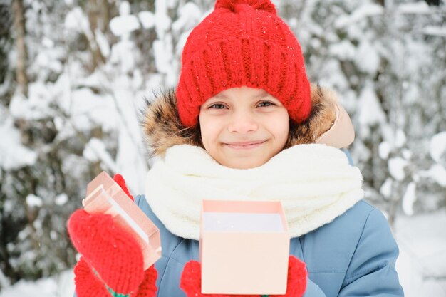 Teen girl gospodarstwa pudełko Boże Narodzenie obecny na zewnątrz dziecko w szalik rękawiczki i santa hat winter park na tle