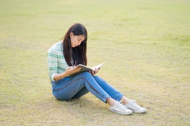 Teenage girl Sitting with guitar Przeczytaj notatnik na trawniku o zachodzie słońca