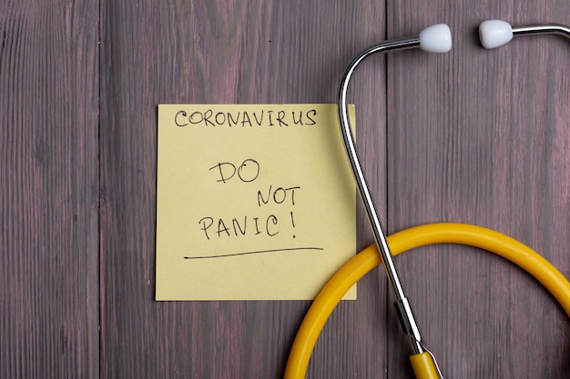 Tekst Don't Panic Coronavirus na karteczce samoprzylepnej i stetoskopie na drewnianym tle
