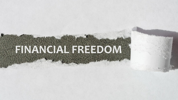 Tekst Financial Freedom pojawiający się za rozdartym białym papierem, szarym tłem, białymi literami, koncepcja biznesowa