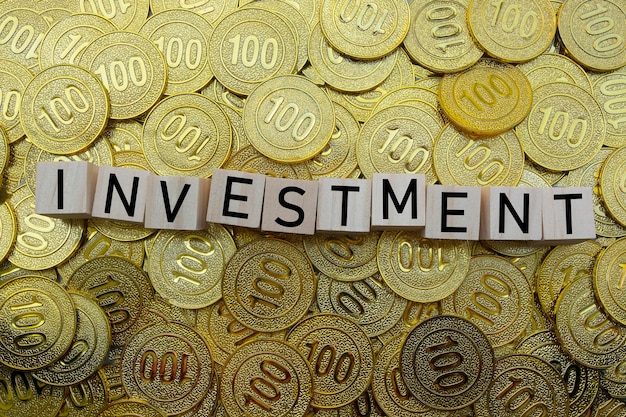 Zdjęcie tekst inwestycyjny na drewnianym bloku ze stosem złotych monet