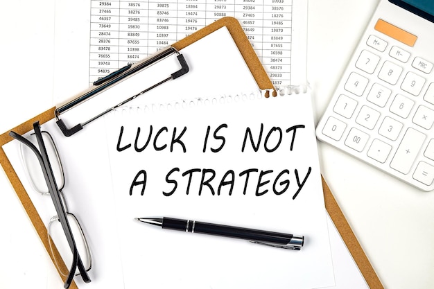 Tekst LUCK IS NOT A STRATEGY na białym papierze w schowku z wykresem i kalkulatorem