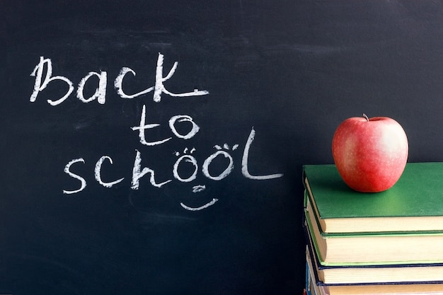 Tekst napis Z powrotem do szkoły na czarnej tablicy i czerwone jabłko na podręczników książek stosu
