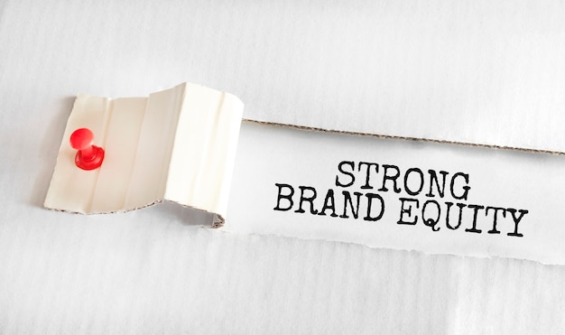 Tekst STRONG BRAND EQUITY znajdujący się za podartym żółtym papierem