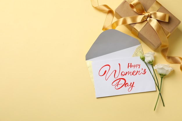 Tekst szczęśliwy dzień kobiet, róże, koperta i pudełko na beżowym tle