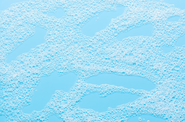 Tekstura białej pianki na niebieskim tle Oczyszczająca pianka do twarzy lub pianka do kąpieli lub proszek do prania Zbliżenie