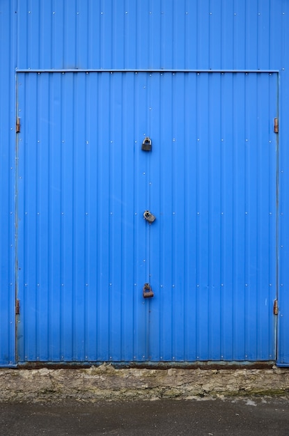 Tekstura metalowej niebieskiej ściany z zamkniętą bramą na trzy zamki