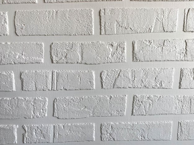 Tekstura powierzchni domowej roboty białej ściany z cegły w stylu loftu z ceglanymi szwami wykonanymi z gipsu