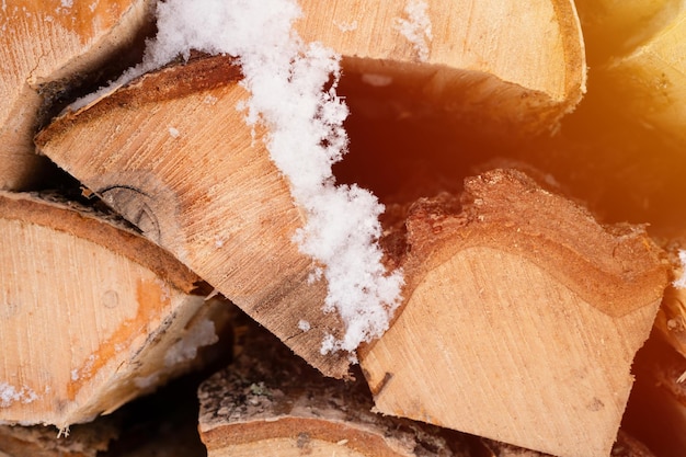 Teksturowane tło drewna opałowego posiekane drewno na rozpałkę stos z ułożonym drewnem opałowym brzoza pokryta świeżym lodowatym mrożonym śniegiem i płatkami śniegu zimna pogoda i śnieżna zima sezon flara