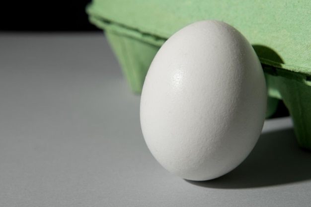 Tekturowe zielone pudełko na jajka na szarym tle, jedno jajko znajduje się poza pudełkiem.