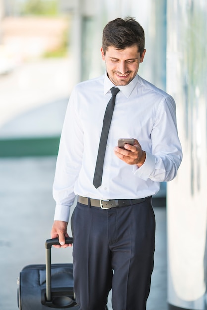 Telefon biznesmena uśmiech i spacer z walizką