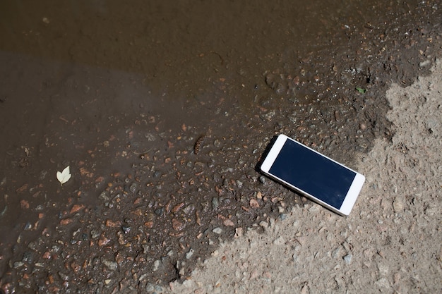 Telefon komórkowy leżący na chodniku w kałuży.