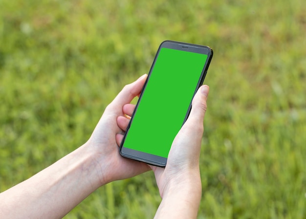 Telefon komórkowy makieta z szablonem zielonego ekranu w kobiecej dłoni nad zielonym trawnikiem smartfon z pustym...