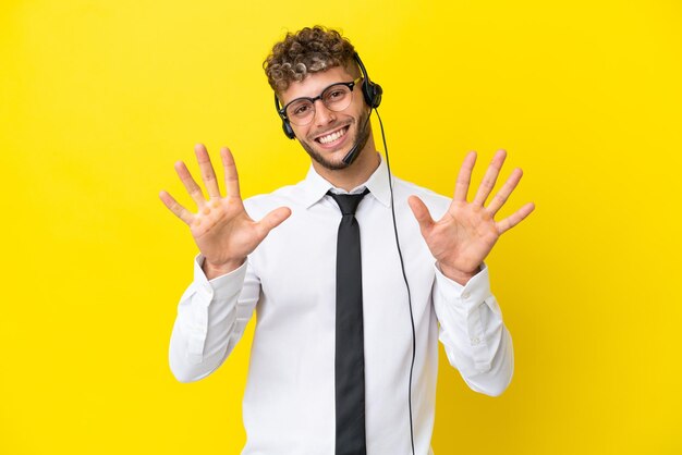 Telemarketer blond mężczyzna pracujący z zestawem słuchawkowym na żółtym tle, licząc dziesięć palcami