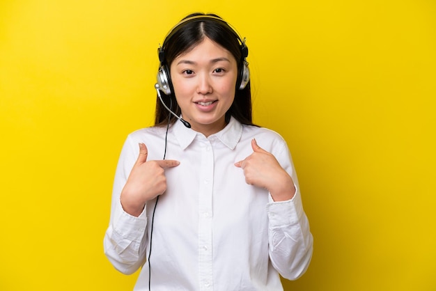 Telemarketer Chinka pracująca z zestawem słuchawkowym na żółtym tle z niespodzianką wyrazem twarzy