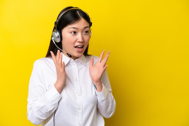 Telemarketer Chinka pracująca z zestawem słuchawkowym na żółtym tle z niespodzianką wyrazem twarzy
