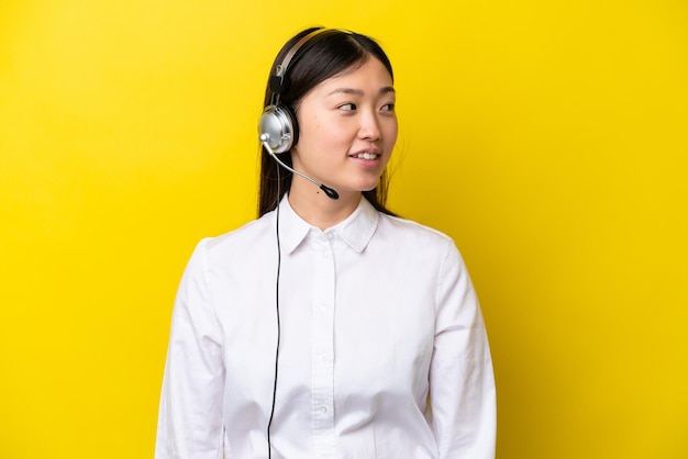 Telemarketer Chińska kobieta pracująca z zestawem słuchawkowym odizolowanym na żółtym tle patrząc z boku
