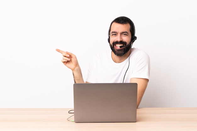 Telemarketer kaukaski mężczyzna pracujący z zestawem słuchawkowym i laptopem wskazującym palcem w bok.