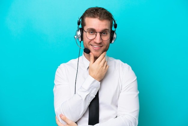 Telemarketer kaukaski mężczyzna pracujący z zestawem słuchawkowym na białym tle na niebieskim tle w okularach i uśmiechnięty