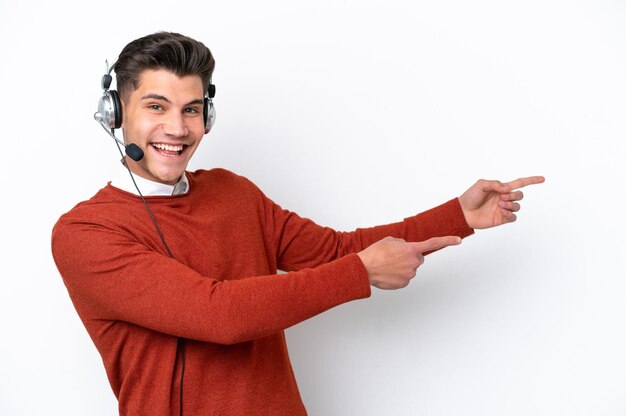 Telemarketer kaukaski mężczyzna pracujący z zestawem słuchawkowym na białym tle wskazujący palec w bok i prezentujący produkt