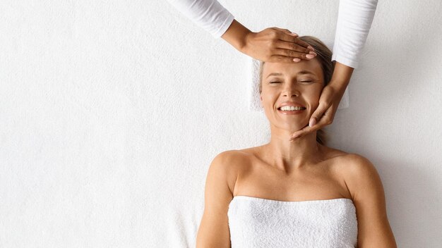 Terapeuta wykonujący masaż twarzy dla pięknej kobiety w salonie spa